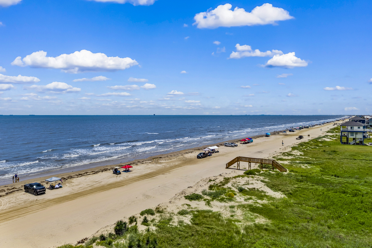 Aerial view of Bolivar Peninsula Texas showing trucks parked on the sand, beach access boardwalk, coastal dunes, and vacation homes along the shoreline