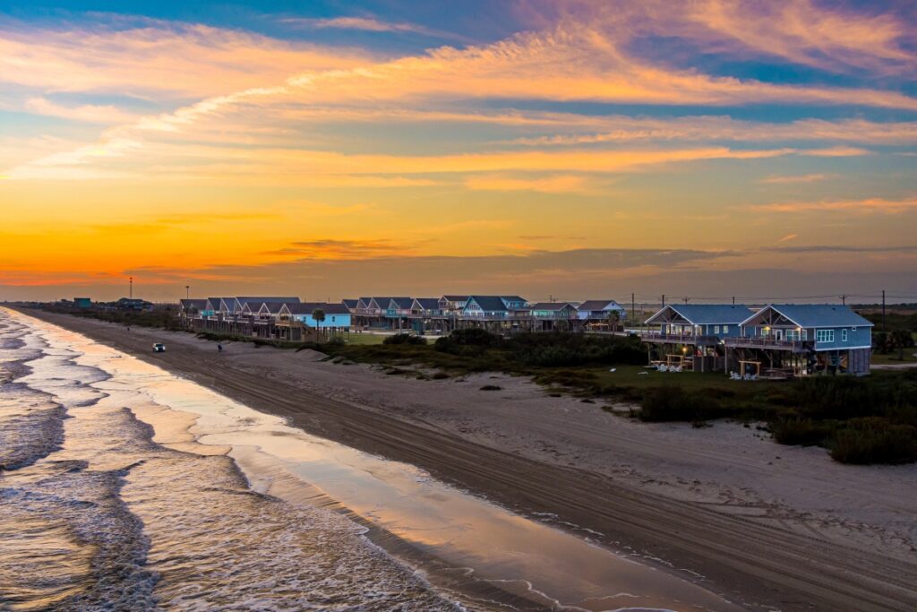 Aerial view of a row of stilted beach houses along a drive-on sand beach at sunset with waves rolling in